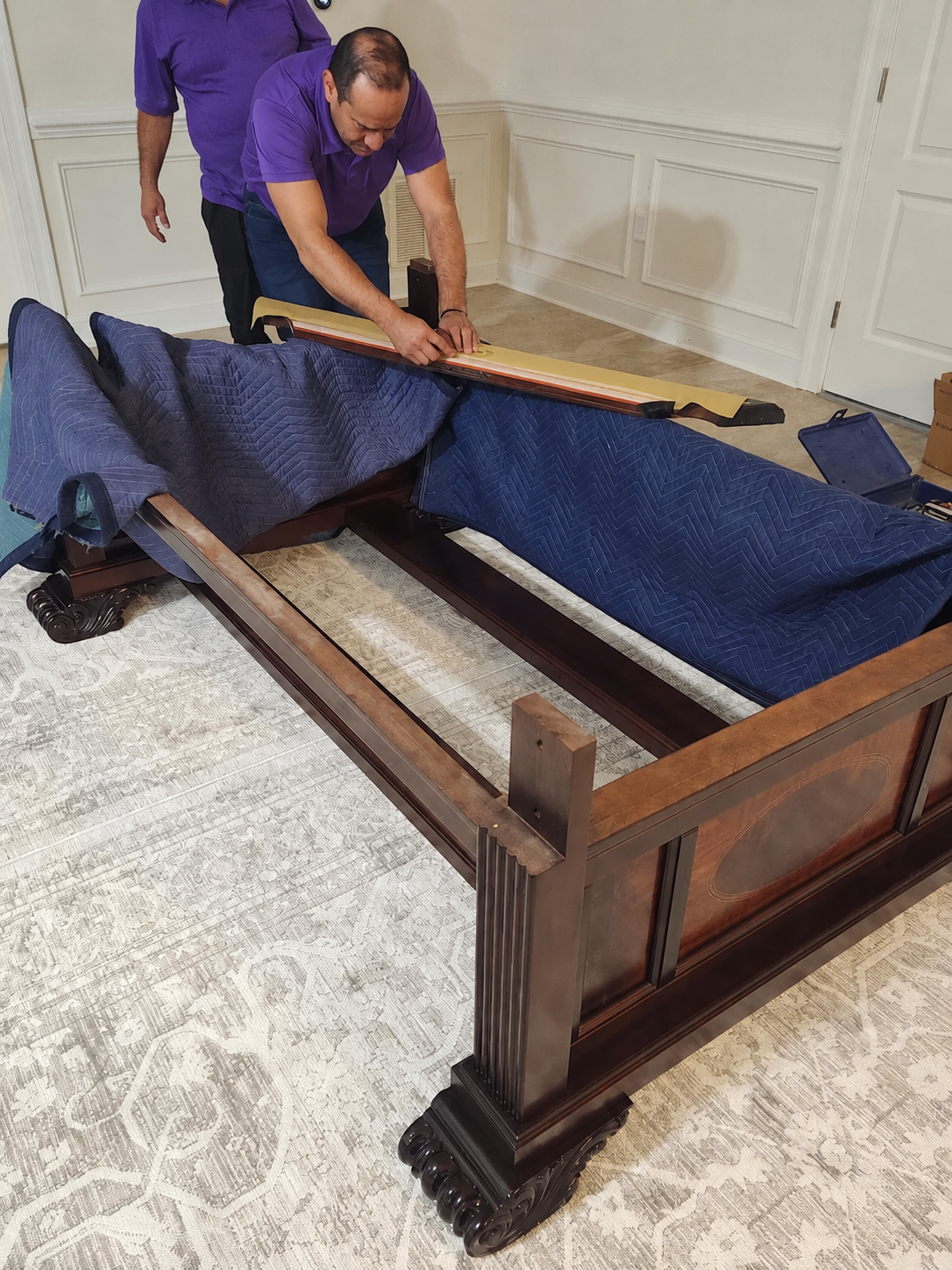 Movers reassembling an antique wood bed frame on moving blankets in Tampa, FL