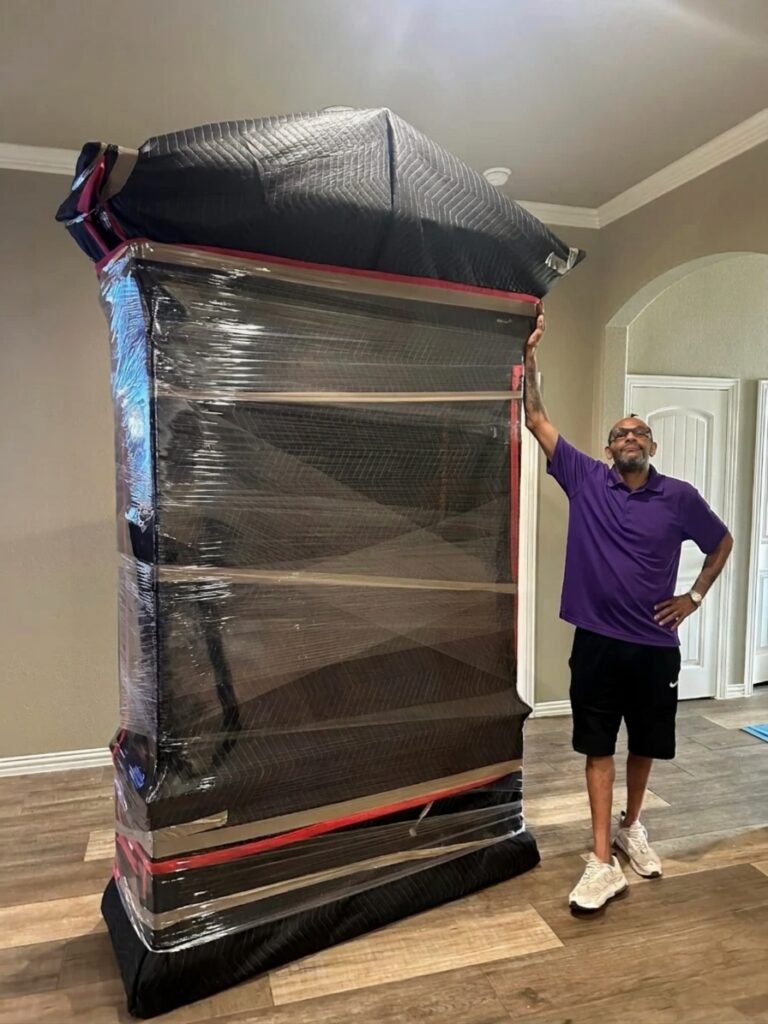 Movers in Lakeview Village, Brandon FL 1 Mover standing next to a tall padded and shrink-wrapped armoire
