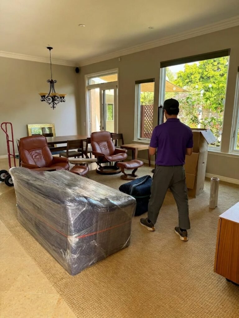 White Glove Movers in Wesley Chapel, FL 1 Mover packing a living room with a wrapped sofa in the foreground in Wesley Chapel, FL