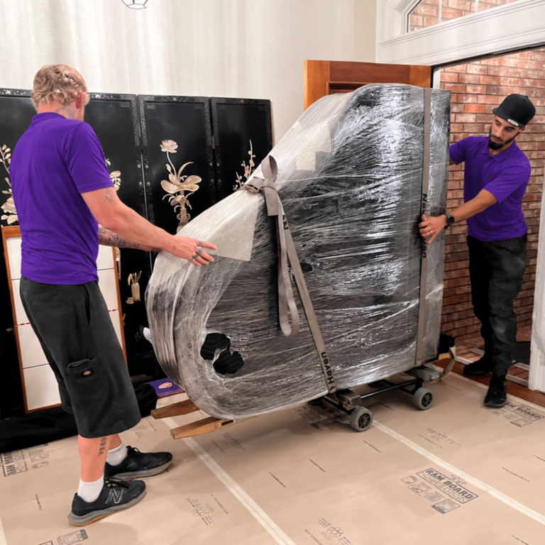 Wesley Chapel Movers 6 Two movers rolling a padded, wrapped grand piano on a piano board over floor protection in Wesley Chapel, FL