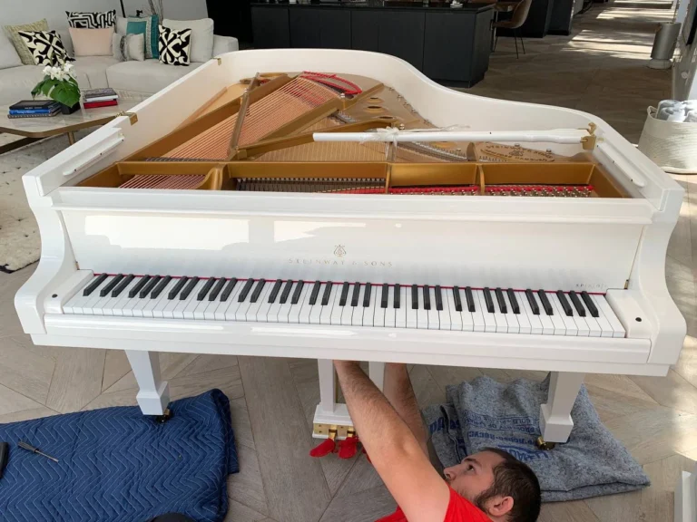 Mover removing the pedal lyre from a white grand piano in Tampa, FL