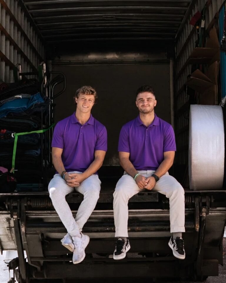Two movers in purple polos sitting on the back of a moving truck in Tampa, FL